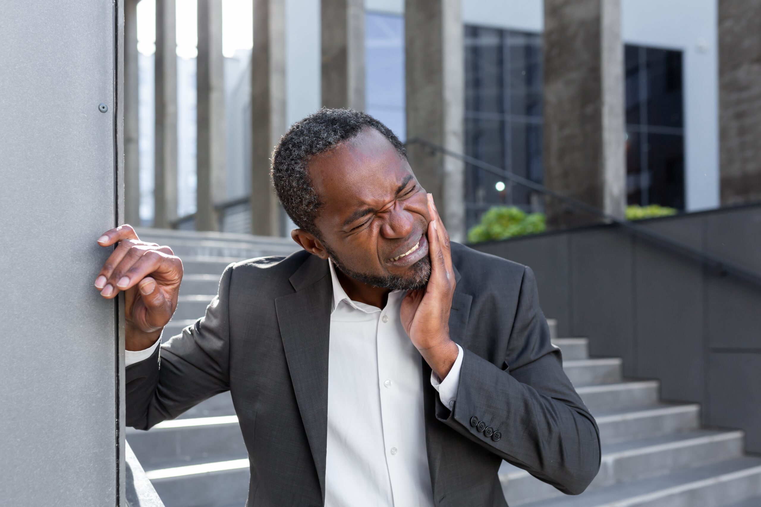 man in a business park wearing a suit and suffering from severe tooth pain, possible dental emergency 