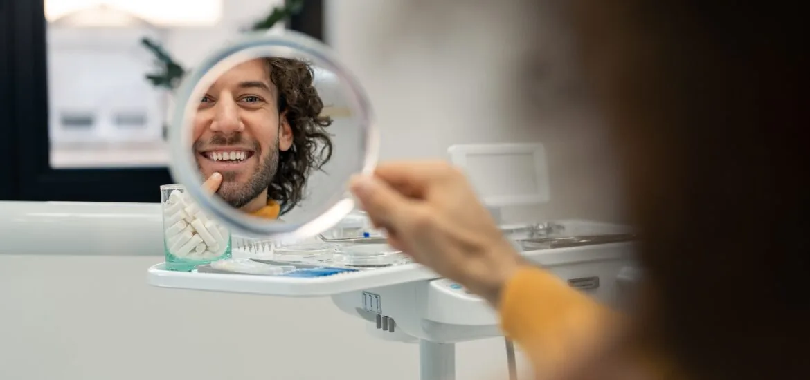 man smiling in a hand mirror, new dental implants