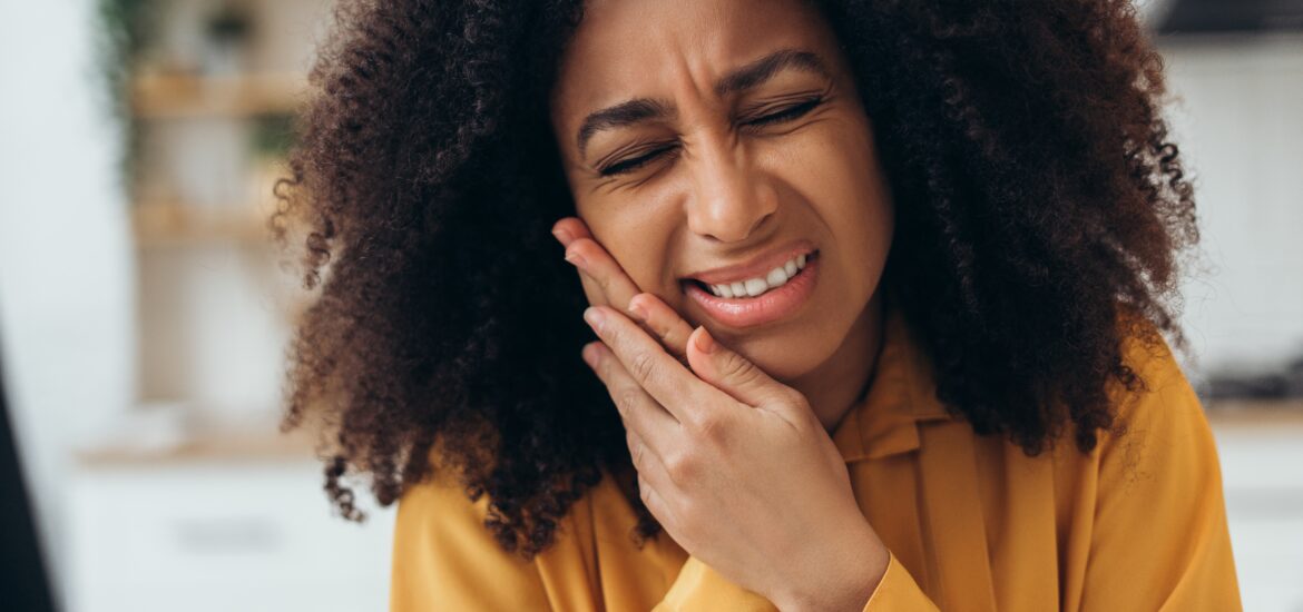young woman in yellow shirt holding jaw, tooth pain, need for root canal