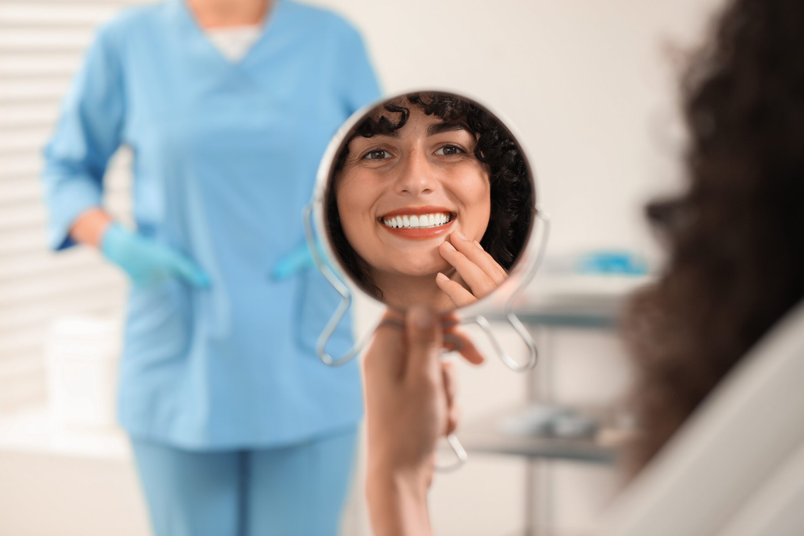young woman smiling in mirror, happy with new dental crown