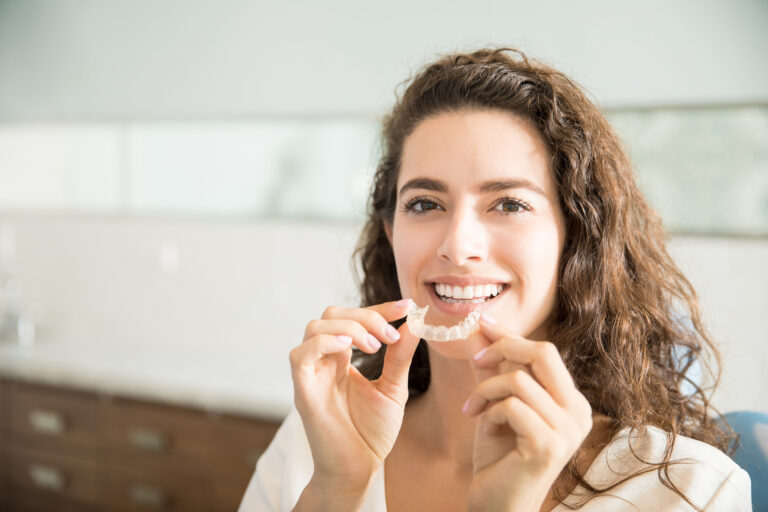 Portrait of beautiful patient holding orthodontic retainers in dental office
