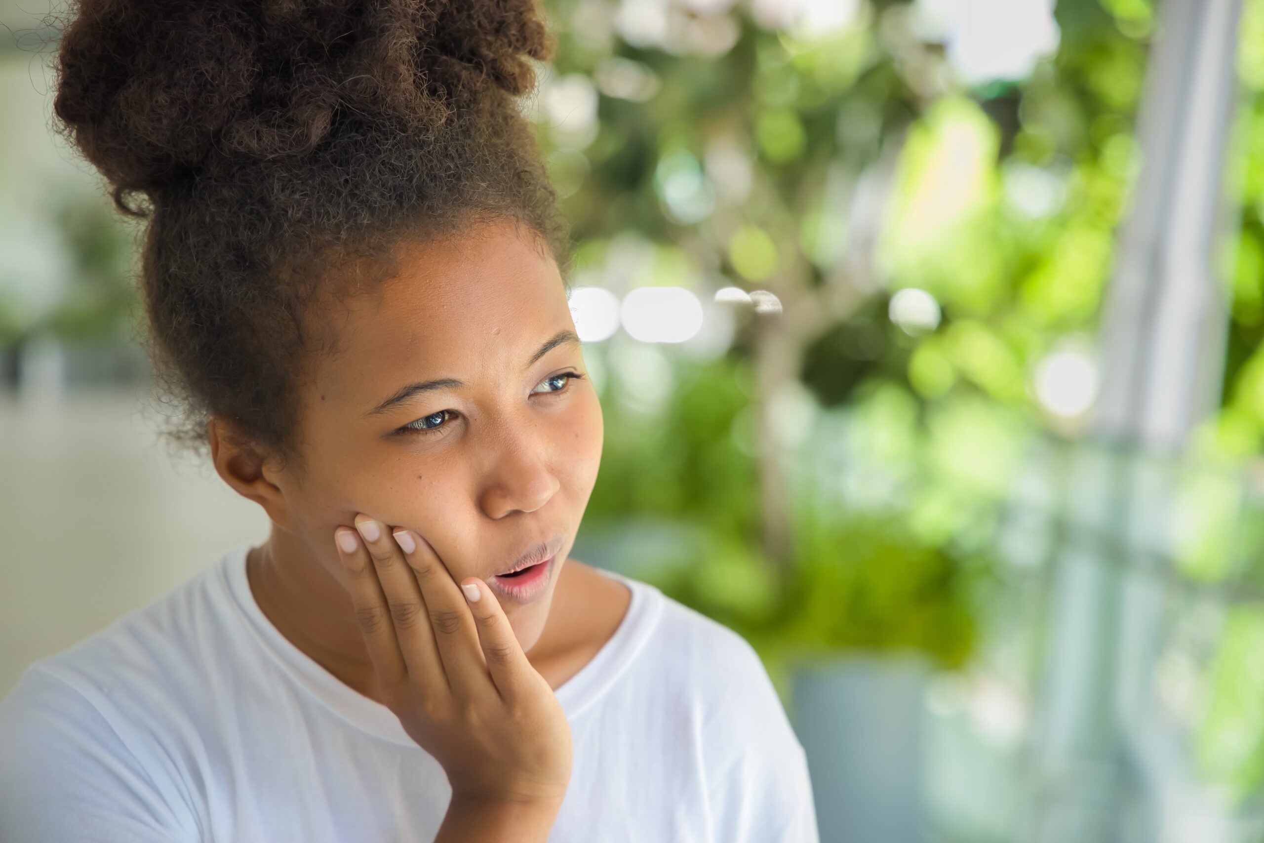 young woman suffering from TMJ related jaw pain, holding her hand to jaw