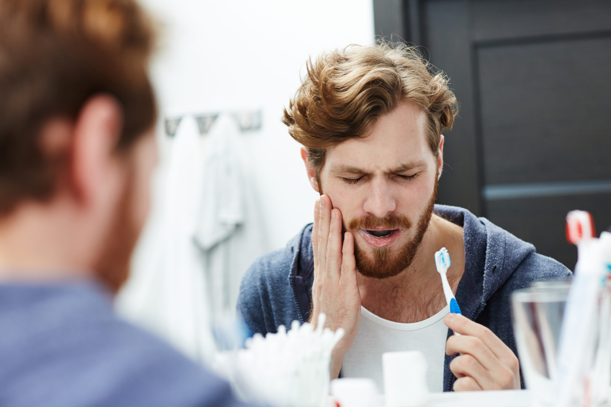 man brushing his teeth in mirror, sensitive tooth pain