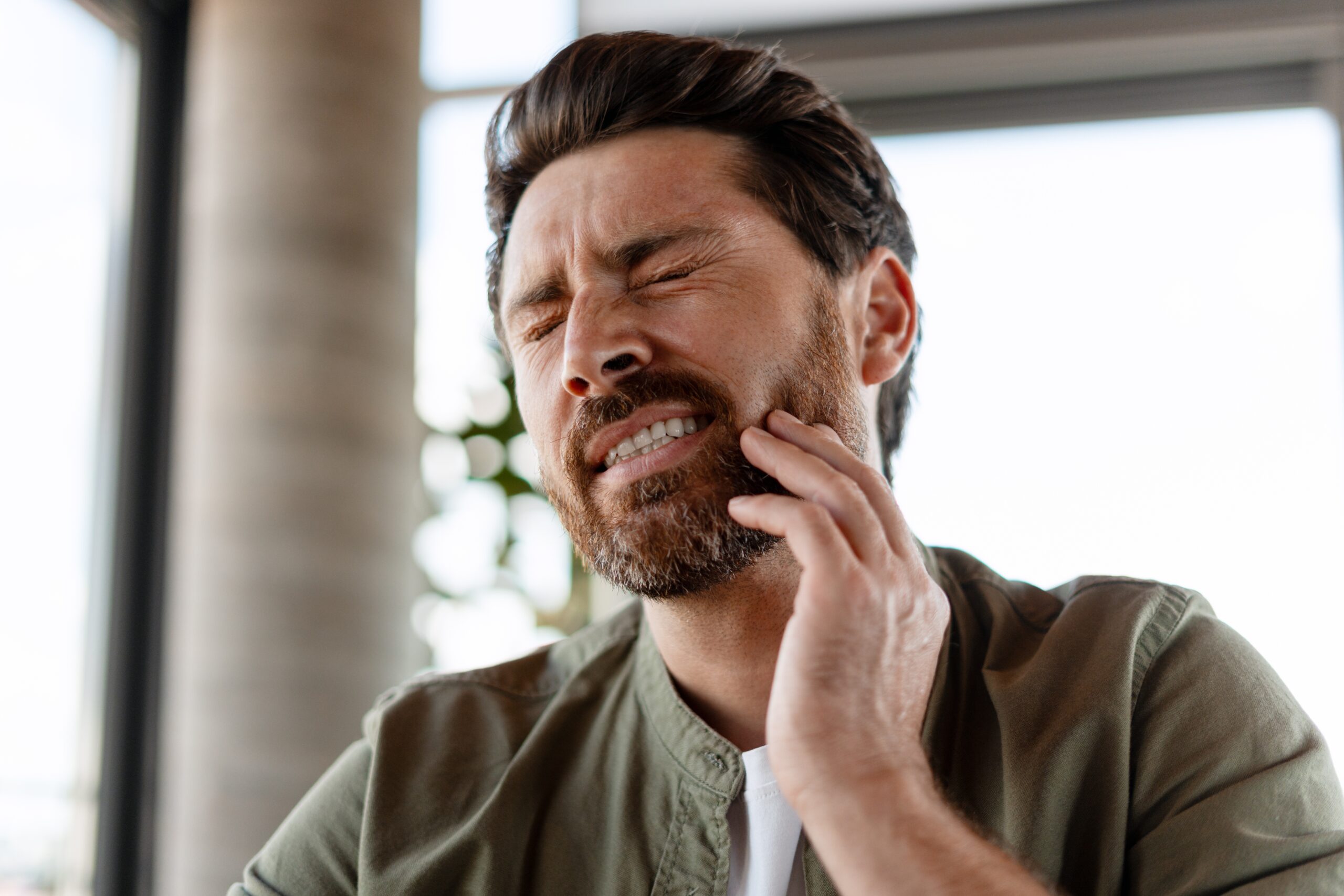 bearded man with severe tooth pain, hand on jaw